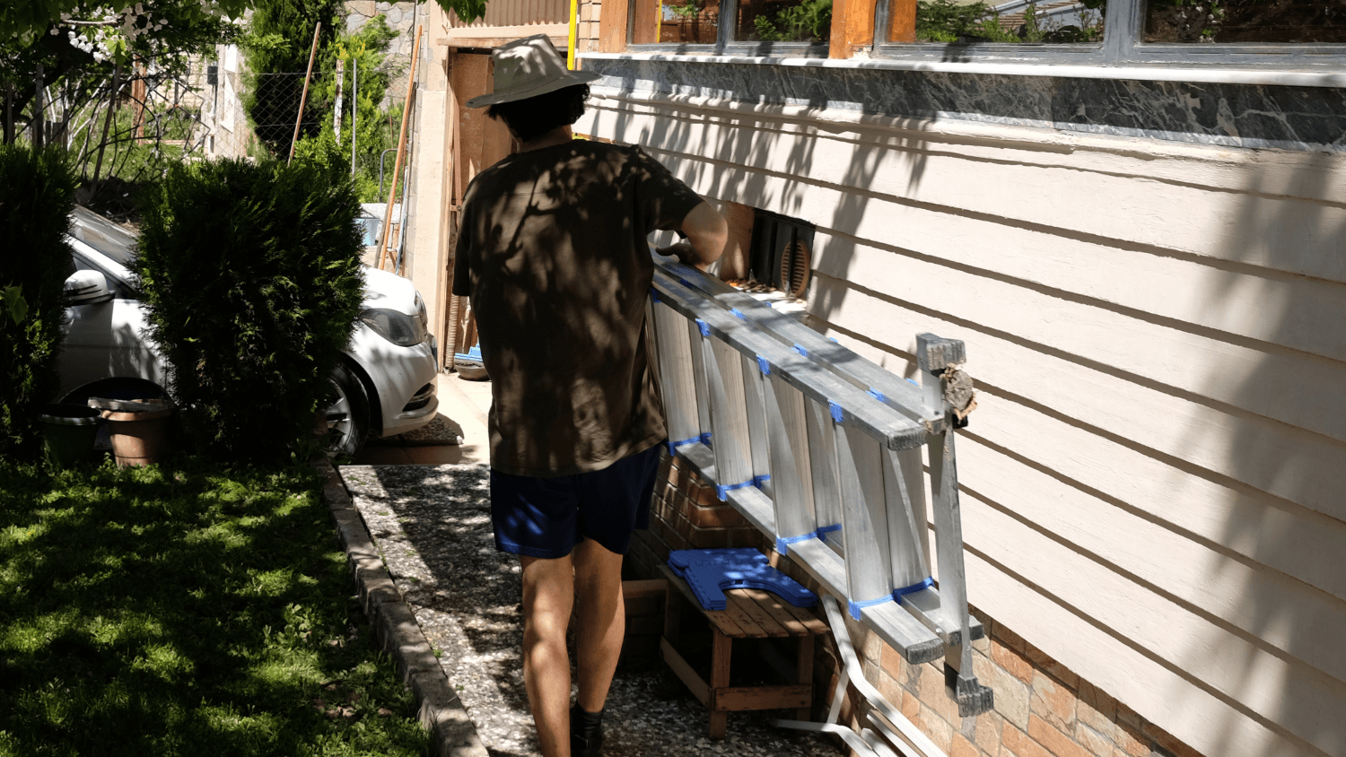 Man carrying ladder around the side of a house